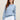 Woman wearing a Thermal Sweatshirt, a light blue cashmere and cotton sweater and white pants against a beige background