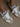 Close up of a person wearing the Cloud Sneaker, a white, beige and gold shoe by Back 70 on a plain white background.