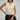 Woman wearing a cream sleeveless Nina Split Neck Tank by Margaret O'Leary against a gray background