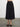 Woman wearing the Natalya Pleated Skirt by Margaret O’Leary, a black pleated midi skirt on a plain background.