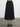 Woman wearing the Natalya Pleated Skirt by Margaret O’Leary, a black pleated midi skirt on a plain background.