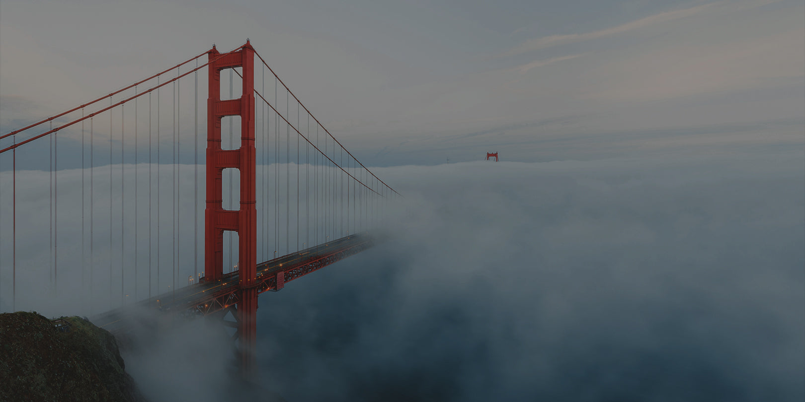 Red Golden Gate Bridge partially submerged in fog with a clear sky above.