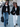 Two women walking on a sidewalk, one in a black jacket and jeans, the other in a black jacket and white pants.