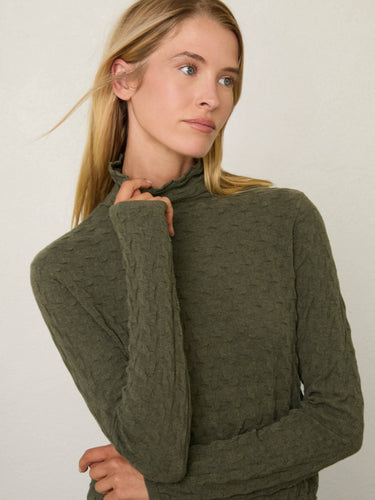 Person wearing the Dimensional Neck, a green tneck textured sweater by Margaret O'Leary paired with blue jeans.