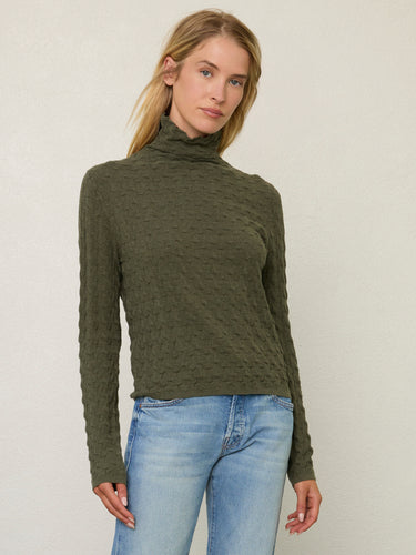 Person wearing the Dimensional Neck, a green tneck textured sweater by Margaret O'Leary paired with blue jeans.