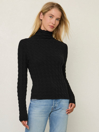 Person wearing the Dimensional Neck, a black tneck textured sweater by Margaret O'Leary paired with blue jeans.