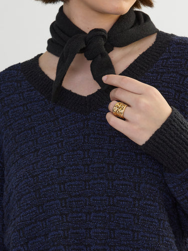 Closeup of a person wearing the Jacquard Vee, a black and blue patterned sweater by Margaret O'Leary paired with black scarf.