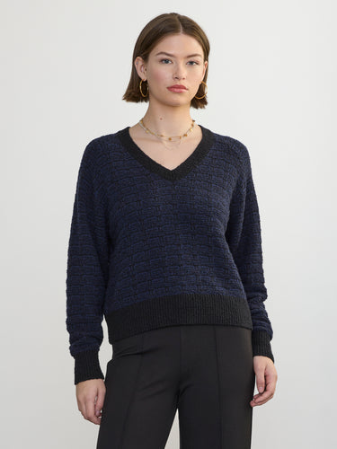 Person wearing the Jacquard Vee, a black and blue patterned sweater by Margaret O'Leary paired with black pants.