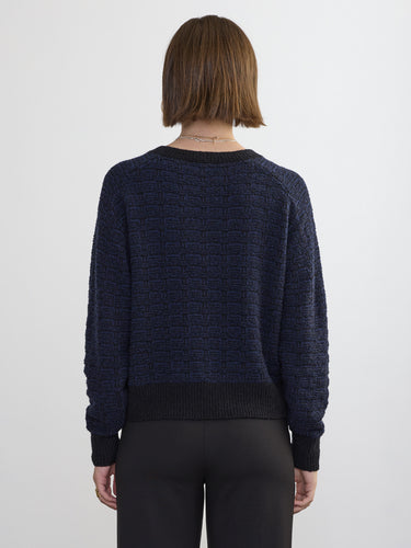 Back view of a person wearing the Jacquard Vee, a black and blue patterned sweater by Margaret O'Leary paired with black pants.