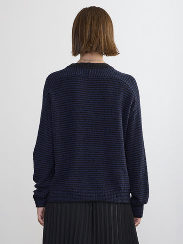 Person wearing the Lola Pullover, a blue and black boucle pullover by Margaret O'Leary paired with a black pleated skirt.