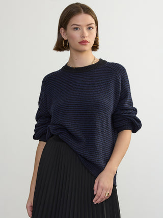 Person wearing the Lola Pullover, a blue and black boucle pullover by Margaret O'Leary paired with a black pleated skirt.