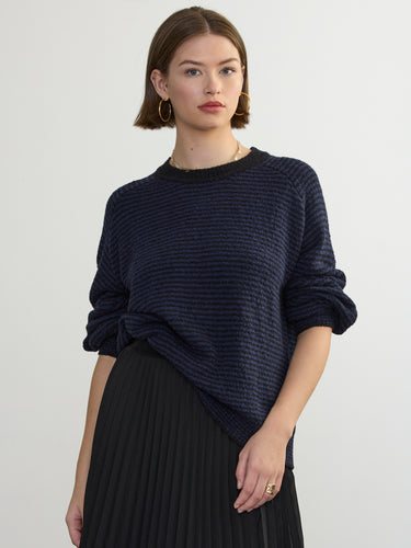 Person wearing the Lola Pullover, a blue and black boucle pullover by Margaret O'Leary paired with a black pleated skirt.