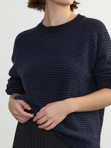 Person wearing the Lola Pullover, a blue and black boucle pullover by Margaret O'Leary paired with a black pleated skirt.