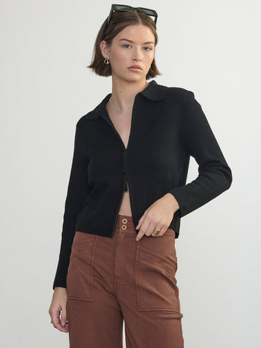 Person wearing the St. Carmel a black waffle knit zip up polo by Margaret O'Leary paired with brown pants.
