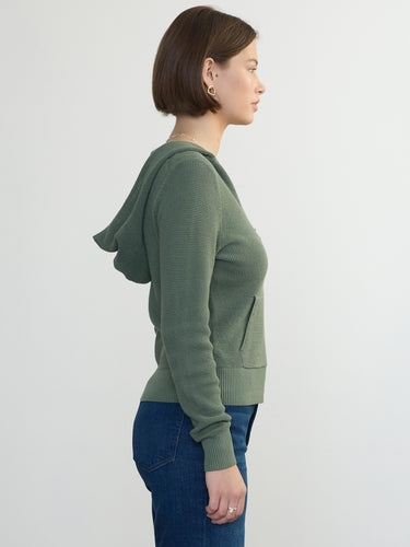 Person wearing the Thermal Hoodie a green waffle knit zip up hoodie by Margaret O'Leary paired with blue jeans.