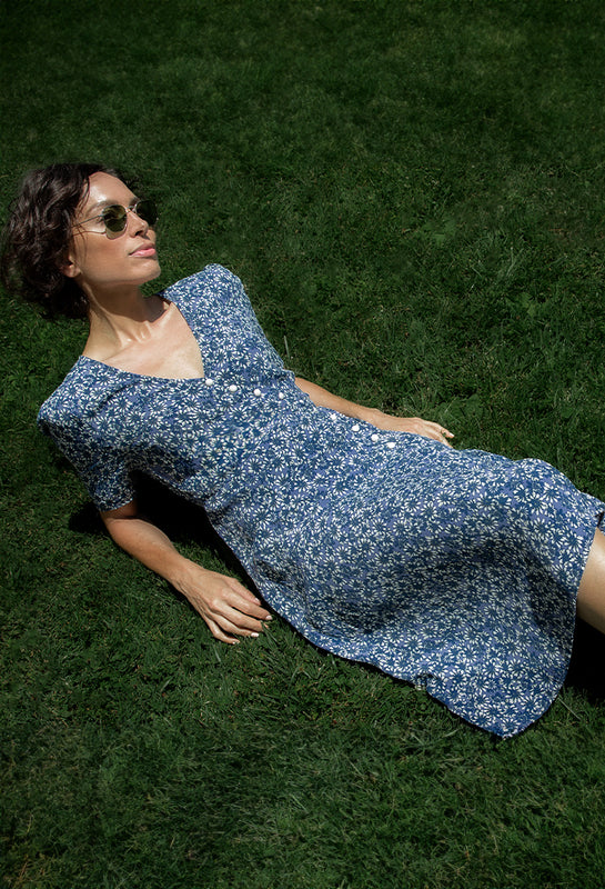 A woman lounging on grass wearing the Daisy Dress by Margaret O'Leary.