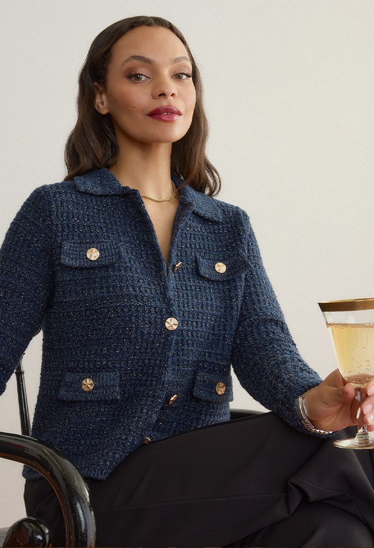 Woman in a blue textured Gabriella jacket by Margaret O'Leary holding a cocktail glass against a plain background