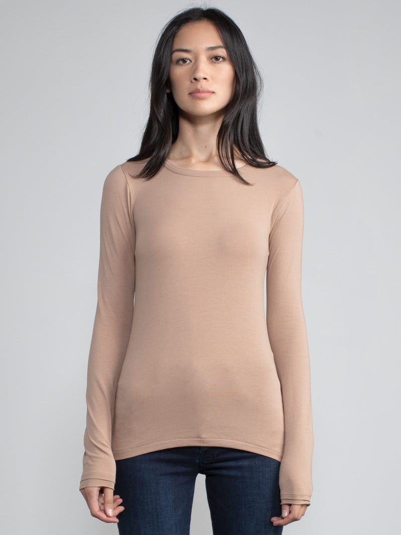 Portrait view of a woman wearing a light brown fitted long sleeve tee.