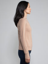 Side view of a woman wearing a light brown fitted long sleeve turtleneck tee.