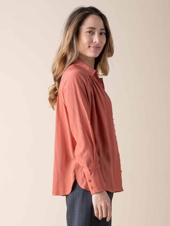 Side view of a woman wearing a silky peach button down blouse.