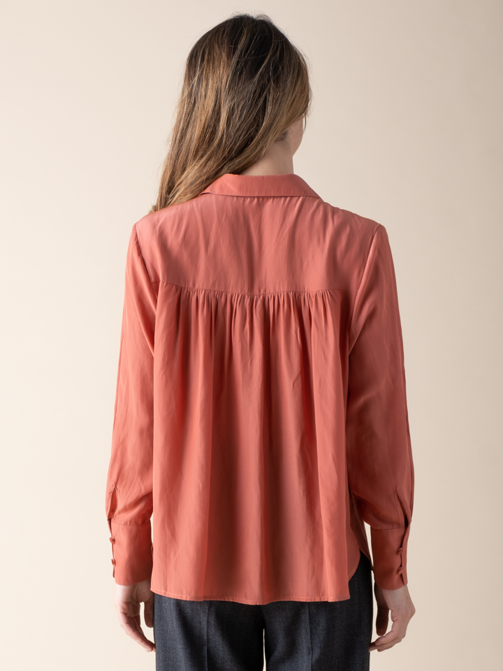 Back view of a woman wearing a silky peach button down blouse.