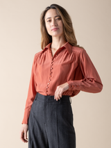 Portrait view of a woman wearing a silky peach button down blouse.