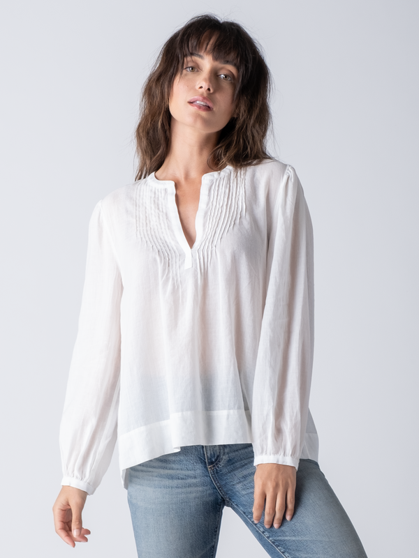 Model wearing a white blouse with pin tuck details near the neckline and a pair of jeans.