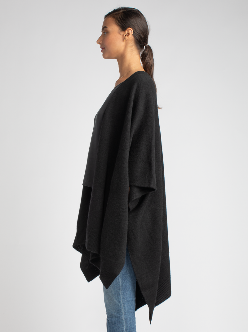Side view: Model wears a white ribbed button up top and a pair of jean with a black cashmere cape.