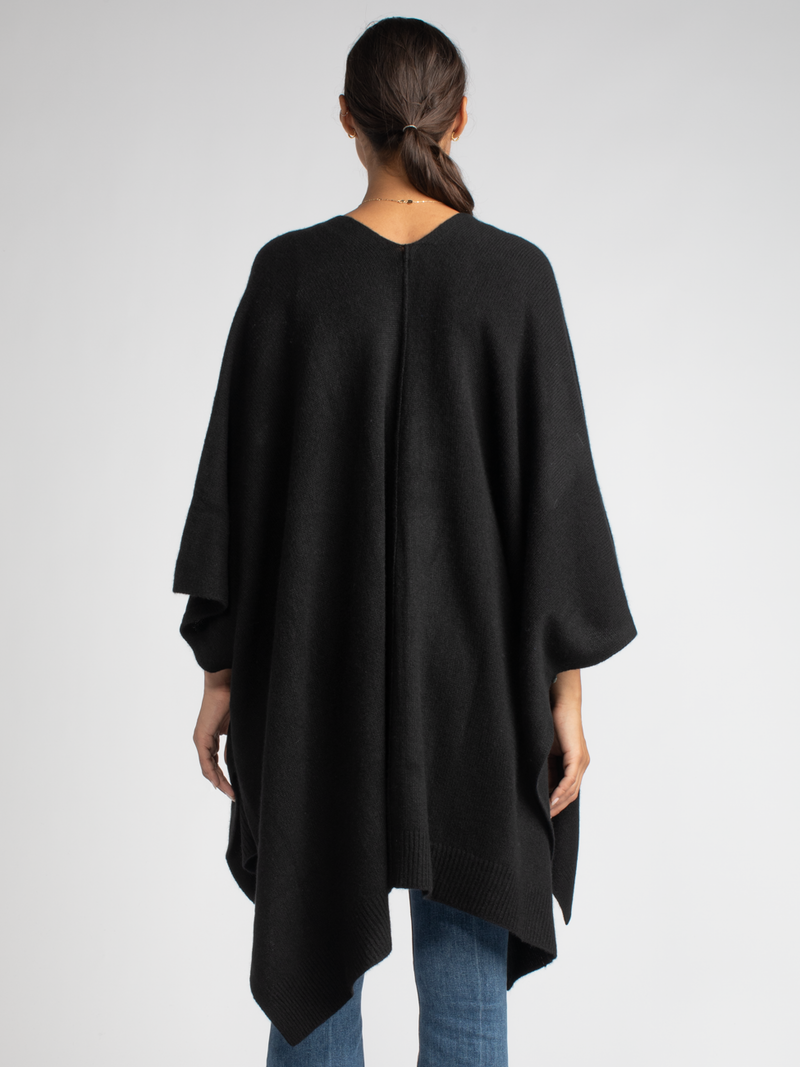 Back view: Model wears a white ribbed button up top and a pair of jean with a black cashmere cape.