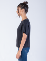 Side view of the model wearing a black silk tee and a pair of jeans.