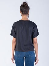 Back view of the model wearing a black silk tee and a pair of jeans.