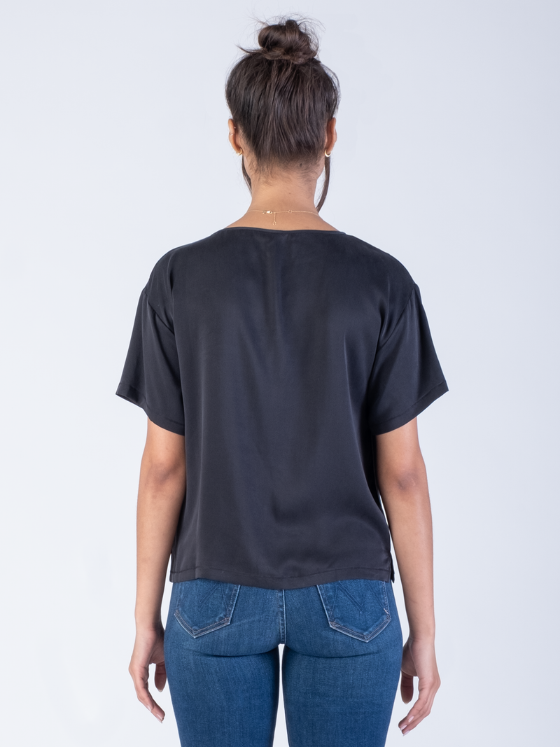 Back view of the model wearing a black silk tee and a pair of jeans.