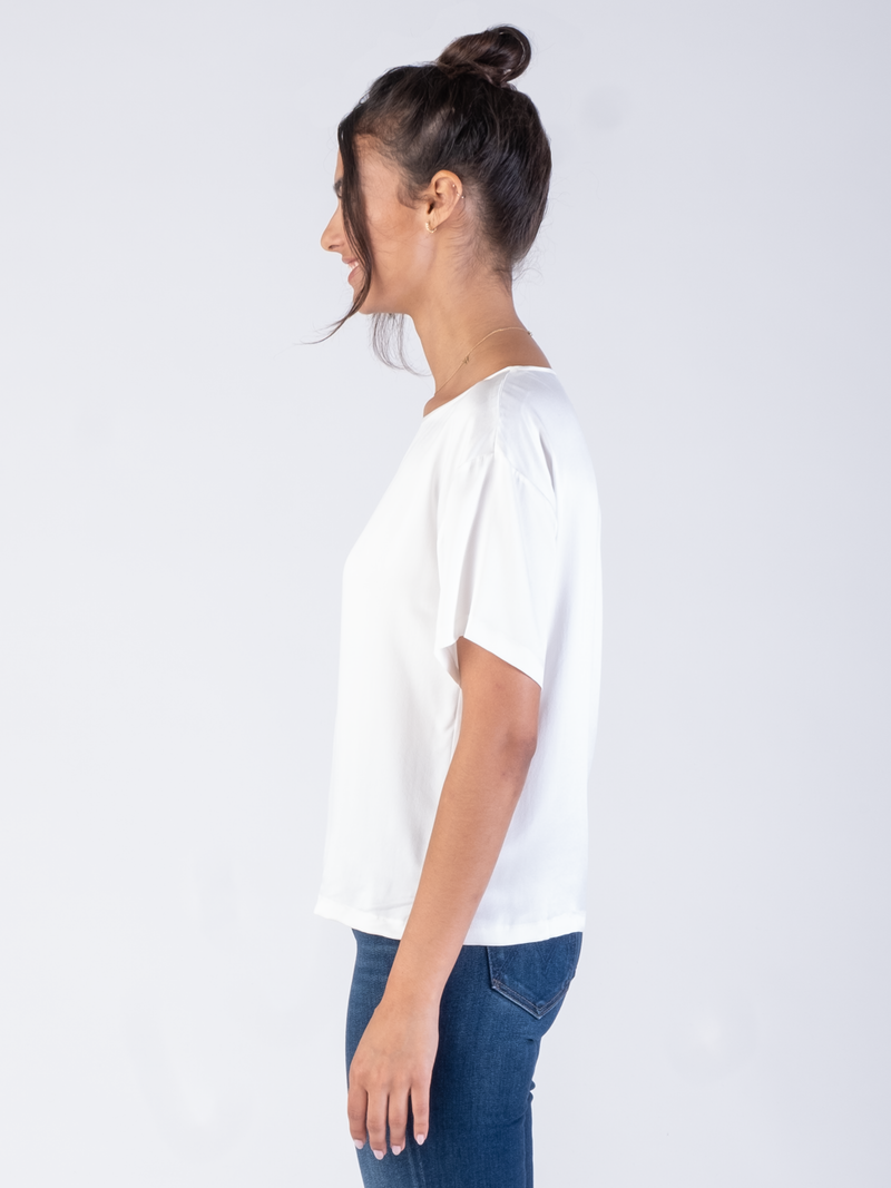 Side view of the model wearing a white silk tee and a pair of jeans.