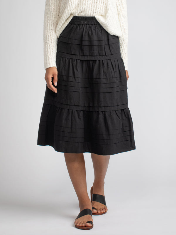 Model wearing a black skirt with horizontal pin tucked details.