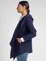 Side view of the model wearing a white shirt underneath a navy cashmere coat and a pair of jeans.