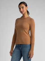 Model wears a tan fitted pullover with thumbholes and ribbed details at the neckline and cuffs and a pair of jeans.