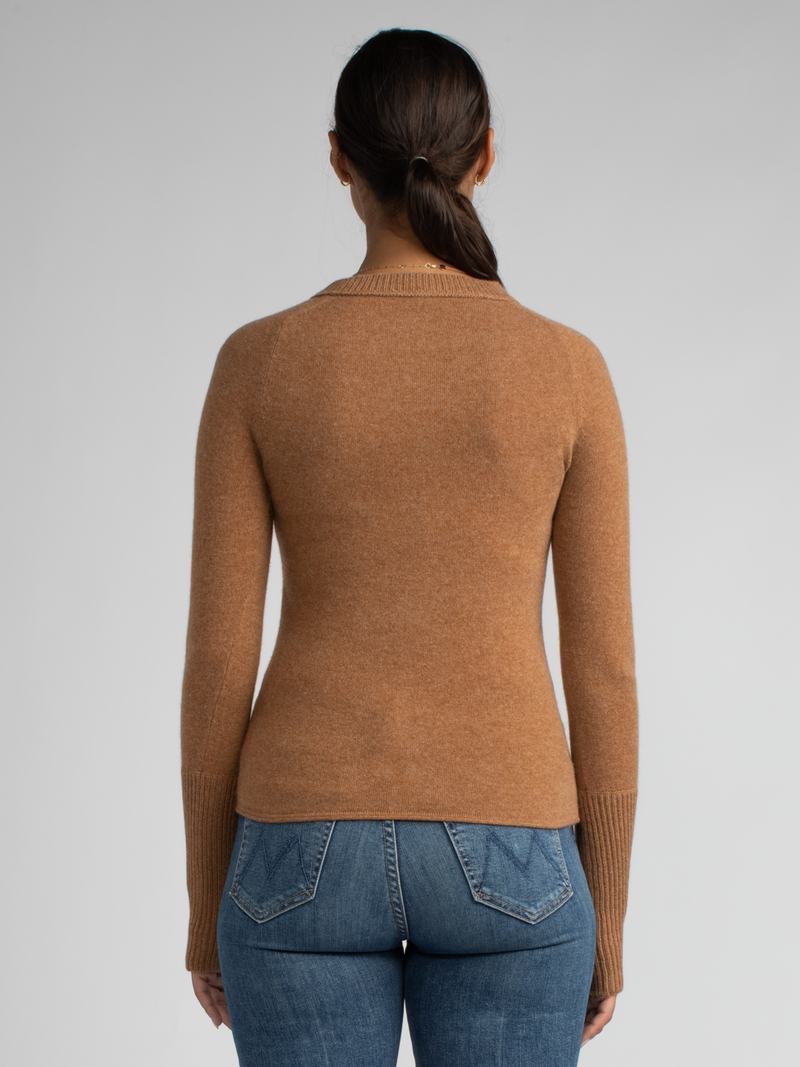 Model wears a tan fitted pullover with thumbholes and ribbed details at the neckline and cuffs and a pair of jeans.