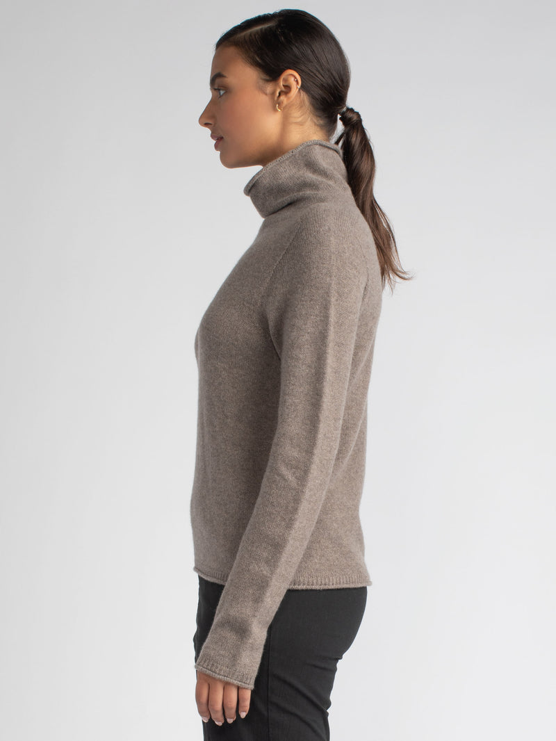 Side view of the model wearing a grain color turtleneck pullover and a pair of jeans.