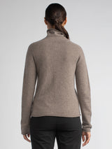 Back view of the model wearing a grain color turtleneck pullover and a pair of jeans.