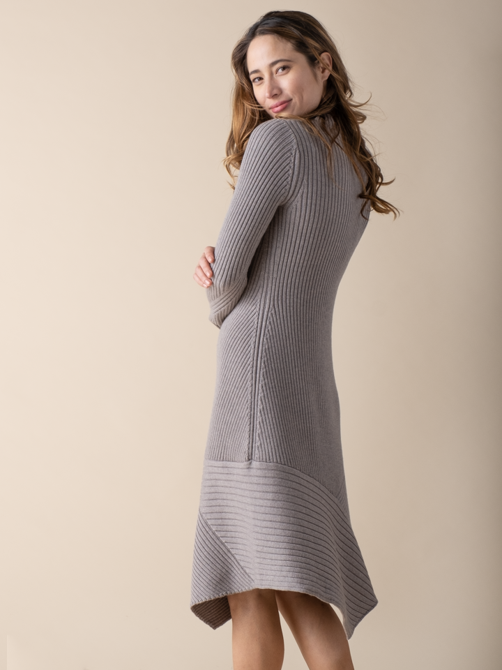 Back view of the model wearing a cement color knit dress and a pair of black boots.