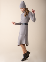 Model wearing a cement color knit dress, a pair of black boots and a grey beanie. Accessorized with a belt.