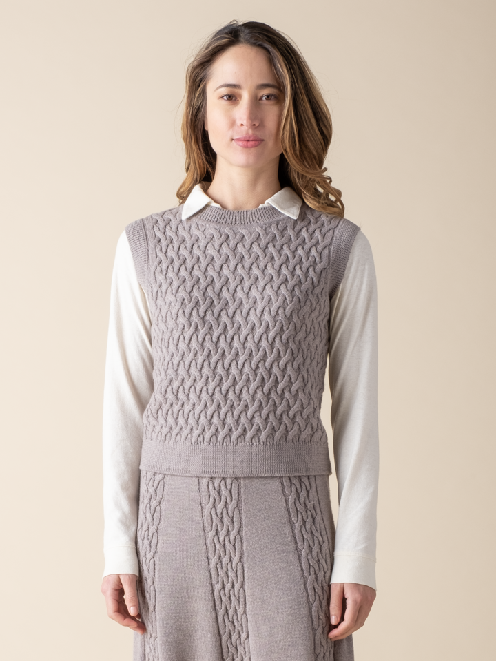 Portrait view of a woman wearing a light grey cable knit sweater vest.