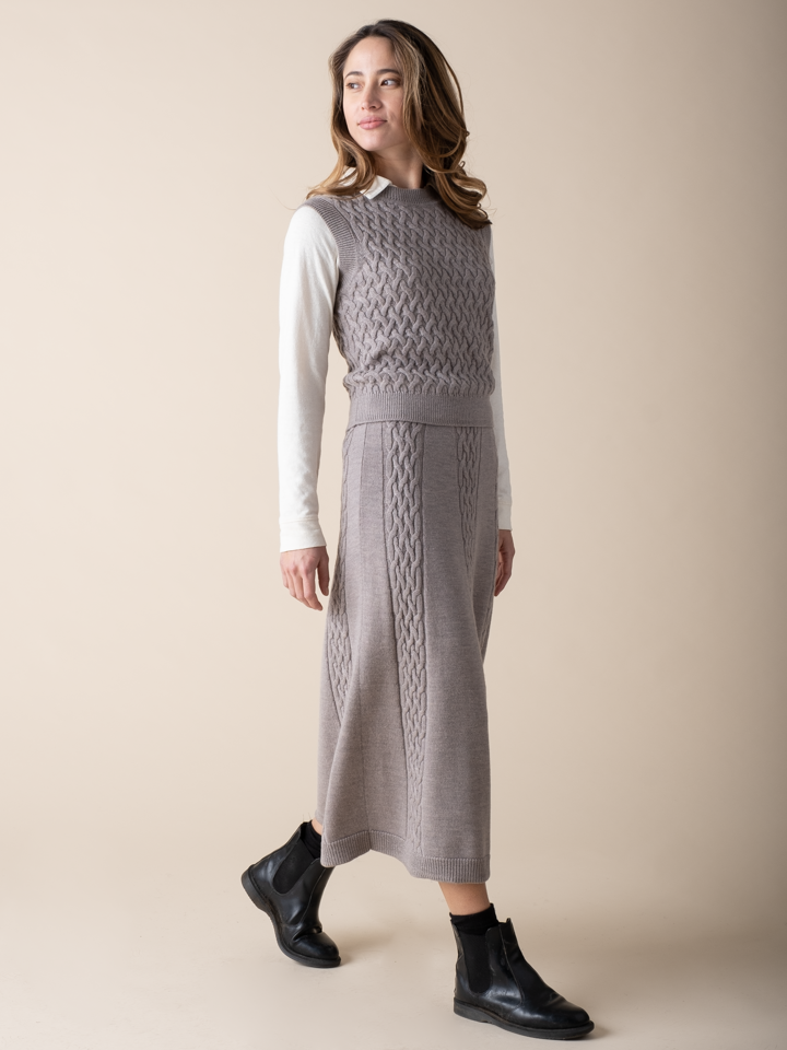 Side view of a woman wearing a light grey cable knit vest and matching cable knit skirt.