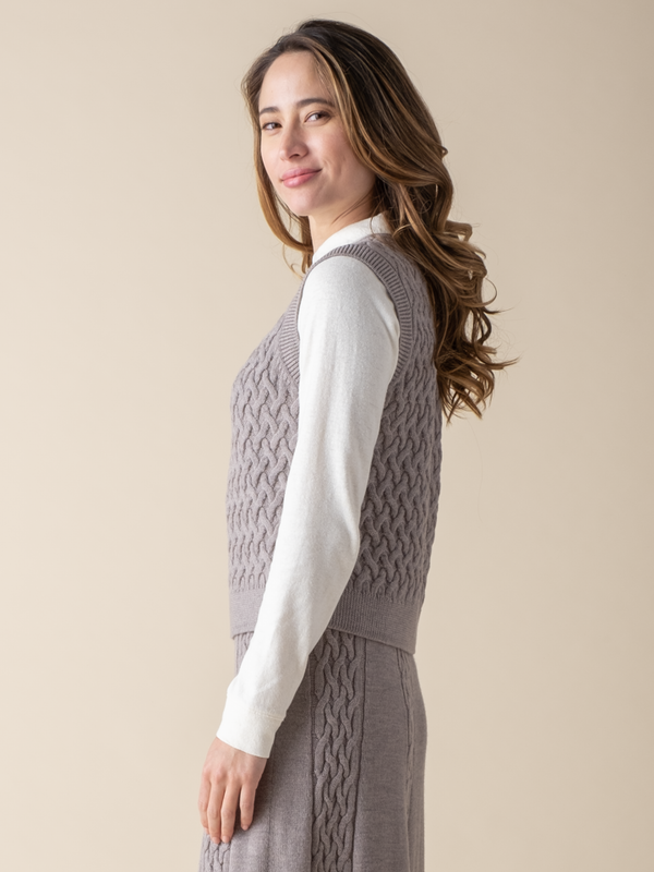 Side view of a woman wearing a light grey cable knit sweater vest.