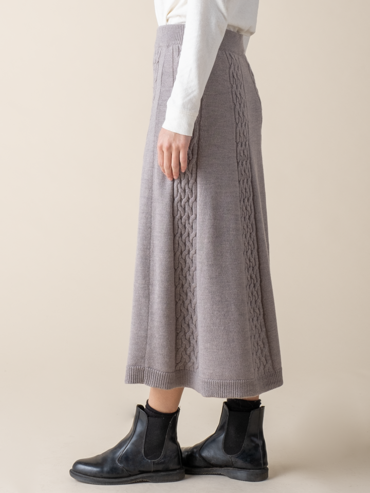 Lower half, side view of a woman wearing a light grey cable knit skirt.