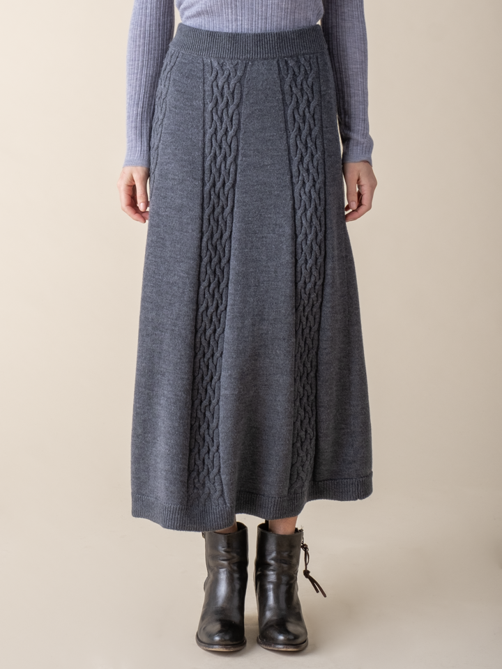 Lower half view of a woman wearing a grey cable knit skirt.