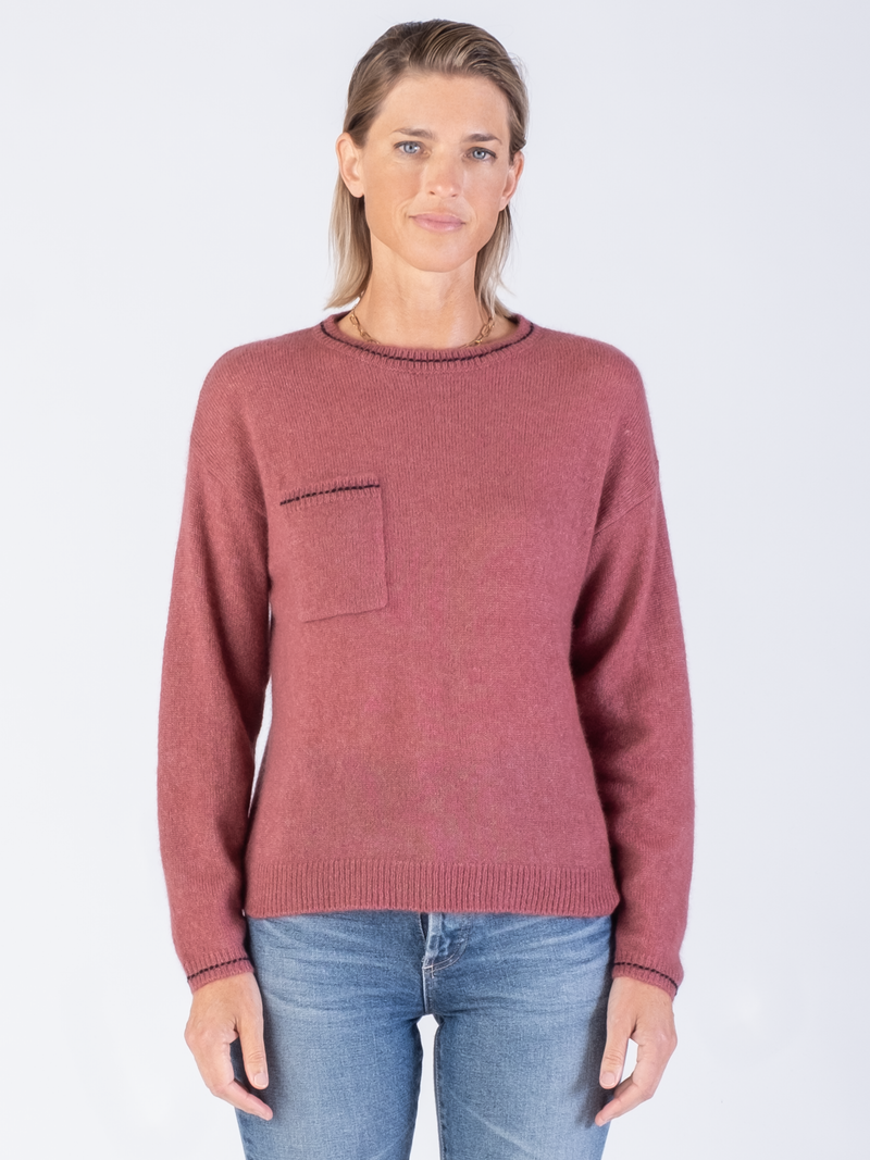 Model wears a pink pullover with black stitching at the edges and a pair of jeans.