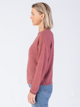 Side view of the model wearing a pink pullover with black stitching at the edges and a pair of jeans.
