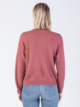 Back view of the model wearing a pink pullover with black stitching at the edges and a pair of jeans.