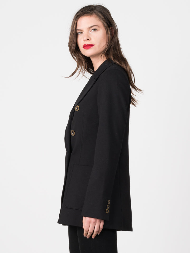 Side view of the model wearing a black peacoat with eight gold circular buttons and two pockets.